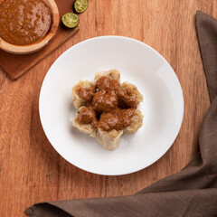 Delicious dumplings topped with a rich sauce sit on a white plate with lime halves nearby on a rustic wooden table