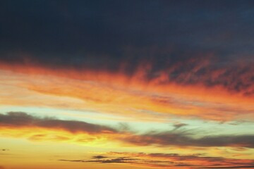 A sunset sky with vibrant hues of orange, pink and purple. The clouds create a dramatic and colorful display. Concept of tranquility of nature. Gradient of colors from deep purple to vibrant orange