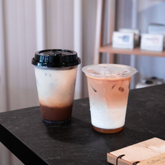 Two iced coffee drinks sit on a dark table in a trendy cafe, showcasing layered beverages under warm afternoon light