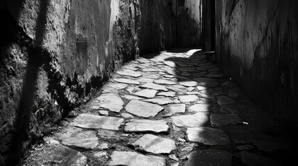 Obraz premium Dimly lit cobblestone path in a shadowy alleyway with uneven pavement and textured stone walls, captured in monochrome.