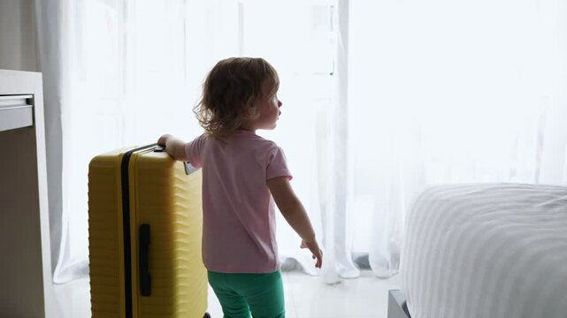 Little girl pulling yellow suitcase in hotel room