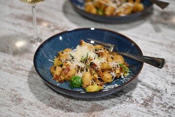 A close-up view of homemade gnocchi served on a blue plate, topped with freshly grated cheese