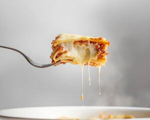 Fork holding a bite of lasagna with cheese stretch and sauce layers in focus, softly lit white background.
