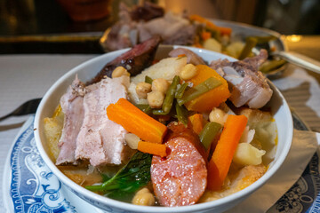 Traditional Portuguese chickpea stew (Cozido de Grão) with chickpeas, vegetables, potatoes, pork, and sausages, served in a rustic restaurant setting, capturing authentic culinary heritage.