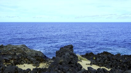Dark volcanic rocks are meeting the deep blue waters of the Atlantic Ocean on a sunny day with some clouds in Charco del Palo, Lanzarote, Canary Islands