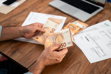 Man holding euro banknotes while calculating utility bills at home. Concept of household expenses,...