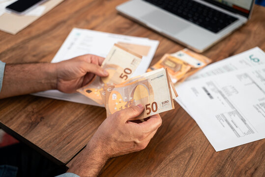Man holding euro banknotes while calculating utility bills at home. Concept of household expenses, tax payments, and online financial management 
