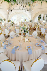 Round banquet table decorated with flower bouquets and blue napkins standing in wedding marquee