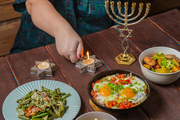 The hand of a Jewish woman lights Shabbat candles at a festive set table