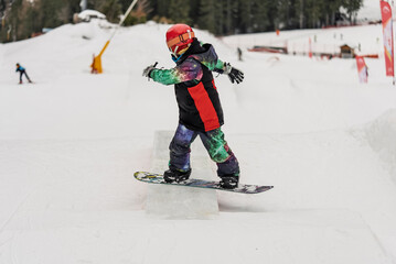 Children in snowpark in Dolomites Alps. Snow park box tricks. Snowboarder in park on a box. Winter jibbing in snwopark. Snowboard lessons on snowpark. Children learn to snowboard with an instructor.
