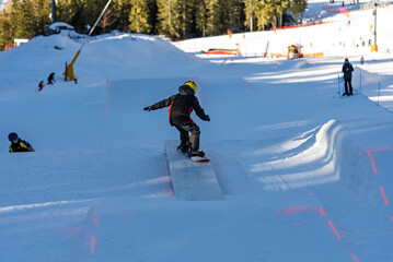 Children in snowpark in Dolomites Alps. Snow park box tricks. Snowboarder in park on a box. Winter jibbing in snwopark. Snowboard lessons on snowpark. Children learn to snowboard with an instructor.