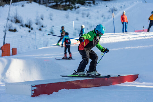 Children skiers in snowpark in Dolomites Alps. Snow park box tricks. Skiers in park on a box. Winter jibbing in snwopark. Ski lessons on snowpark. Children learn to ski with an instructor.