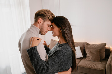 A couple sharing an intimate moment while standing in a warmly lit living room. The scene conveys...