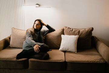 A woman comfortably seated in a warm and cozy environment with contemporary decor, exuding a sense...