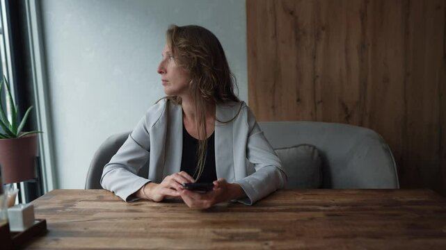 Woman in a cafe waiting for a meeting, looking around while checking her phone.