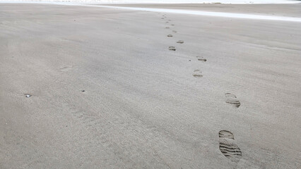 Lonely shoe prints on sand , empty beach. Cloud dancer color of 2026