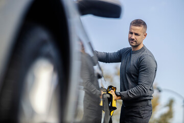 A young man is polishing and cleaning his car at car wash with microfiber cloth.