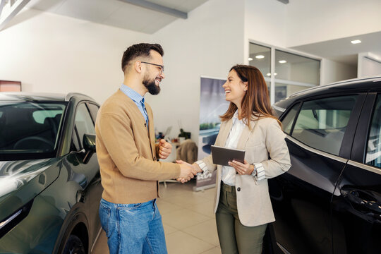 Car saleswoman shaking hands with customer in luxury car salon. - Powered by Adobe