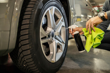 Cropped picture of unrecognizable man spraying tire rims with rim solution and cleaning it.