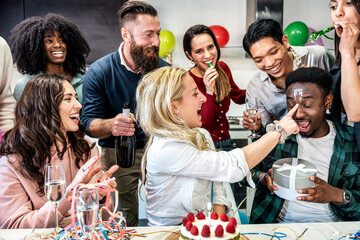 Group of happy people celebrating diverse birthday among friends smiling while having a party - Girl smearing cake on boy's face - Celebration, anniversary and bday concept with friends make a wish