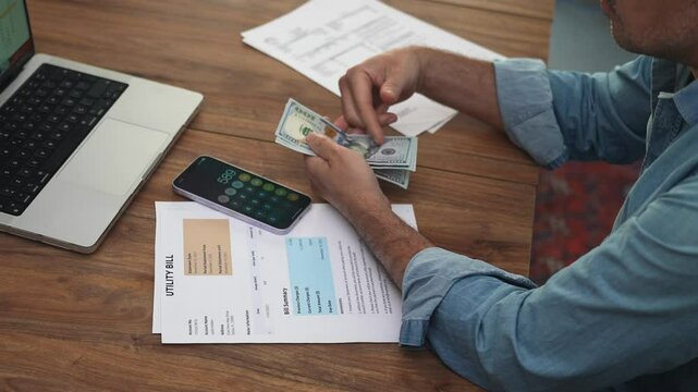 Old gentleman in shirt counts folded stack of dollar bills in hands, cash re-discount against calculator and scattered financial documents on office table slow motion
