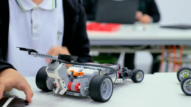 Close-up of a group of children assembling a robot from plastic parts programmed on a computer at a robotics school, the robot moves on a table. Creative kids working on the tech project at school.