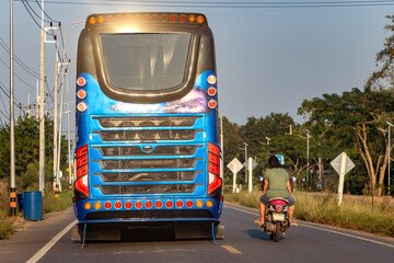 A couple on a motorbike overtakes a tourist bus on a country road, Thailand