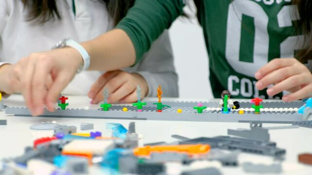 Close-up of a group of children assembling a robot from plastic parts programmed on a computer at a robotics school, the robot moves on a table. Creative kids working on the tech project at school.