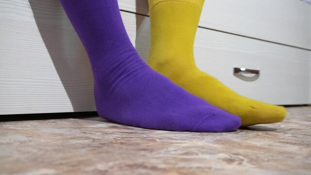 Feet wearing mismatched colorful socks resting on the floor. A crossing legs wearing odd socks: purple and yellow. Different socks as symbol of down syndrome.