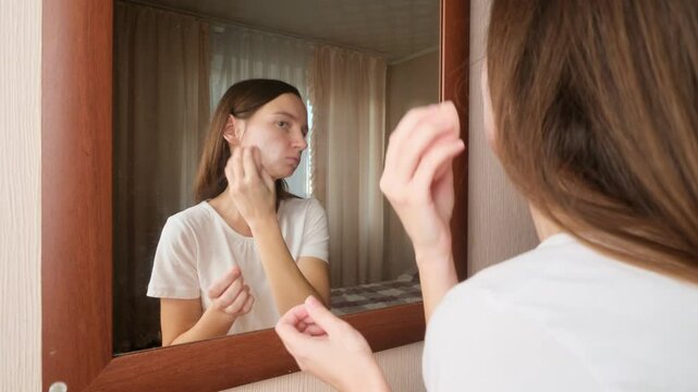 Young woman applying cosmetic foundation with applicator near mirror indoors. Female using decorative makeup at home