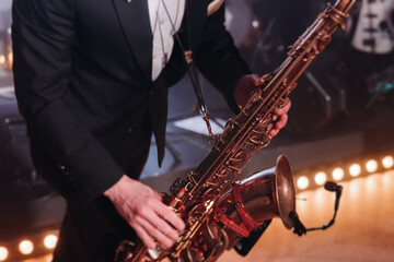 Fototapeta premium Concert view of saxophonist musician, saxophone sax player with vocalist and musical band during jazz orchestra show performing music on a stage in the scene lights, concert in a musical club hall