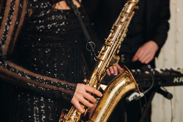 Fototapeta premium Concert view of female saxophonist musician, saxophone sax player woman with vocalist and musical band during jazz orchestra show, performing music on a scene in the stage lights in a musical club
