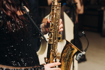 Naklejka premium Concert view of female saxophonist musician, saxophone sax player woman with vocalist and musical band during jazz orchestra show, performing music on a scene in the stage lights in a musical club