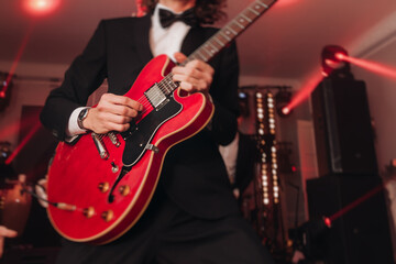 Concert view of an electric guitar player with vocalist and rock band performing in a club, male...