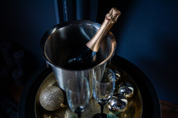 Stylish New Year celebration setup with a champagne bottle in a silver ice bucket, two elegant glasses, gold ornaments, and pine branches on a golden tray, set against a dark, luxurious background