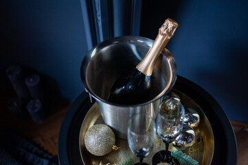 Stylish New Year celebration setup with a champagne bottle in a silver ice bucket, two elegant glasses, gold ornaments, and pine branches on a golden tray, set against a dark, luxurious background