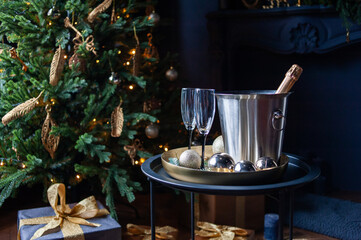 Stylish New Year celebration setup with a champagne bottle in a silver ice bucket, two elegant glasses, gold ornaments, and pine branches on a golden tray, set against a dark, luxurious background