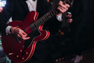 Obraz premium Concert view of an electric guitar player with vocalist and rock band performing in a club, male musician guitarist on stage with audience in a crowded concert club hall arena, hands on a guitar
