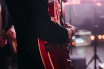 Concert view of an electric guitar player with vocalist and rock band performing in a club, male musician guitarist on stage with audience in a crowded concert club hall arena, hands on a guitar