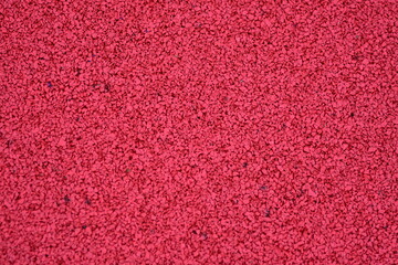 Red sports field rubber coating close up. Playground paving background texture.