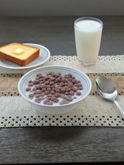 Breakfast with Chocolate Cereal in Milk, Buttered Toast, and Glass of Milk on a Rustic Farmhouse Table