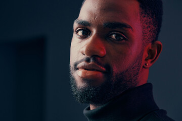 A close up portrait of a young Black man with a stylish beard, wearing a high neck black sweater,...