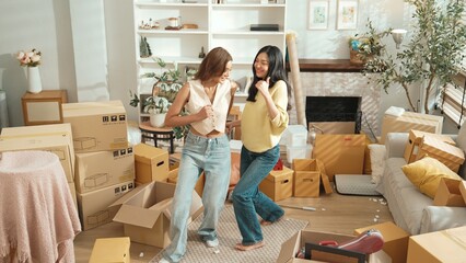 Happy lesbian lover dancing together at living room in moving day. Couple of friend moving to music and perform freestyle dancing at living room with cardboard box scattering. Relocation. Myrmidon.