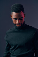 Fototapeta premium A thoughtful young African man in a black turtleneck sweater looking down against a dark gradient background, conveying introspection and calm emotions
