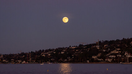 A full moon rising on the horizon and reflecting its glow on the waters of Lake Geneva, in Switzerland