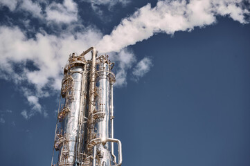 Distillation column releasing steam at a chemical plant under a clear blue sky during daylight