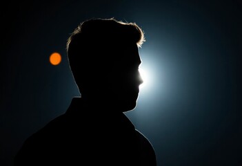 Silhouette of a male person in shadows with backlighting creating an enigmatic ambiance in an unknown location at twilight.