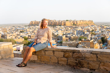 Fototapeta premium Young blonde European woman travelling in Rajasthan, enjoying panoramic view of Jaisalmer city fort, India