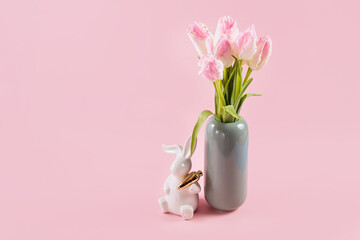 Beautiful pink tulips in vase and white Easter bunny figurine on pastel pink background. Happy...