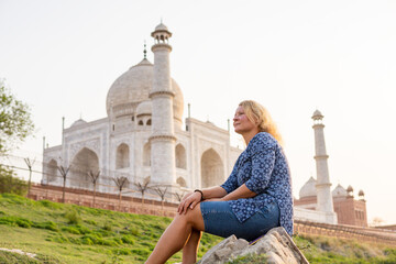 Blonde woman enjoying sunset on the banks of Yamuna river with the view over the ivory-white marble...